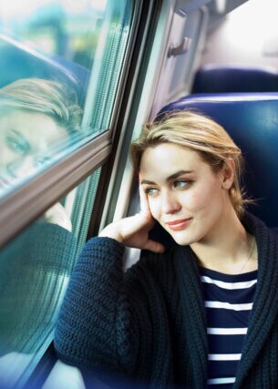 Eine Frau sitzt im Zug und schaut aus dem Fenster.