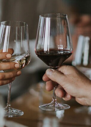 Nahaufnahme von zwei Personen, die jeweils ein Glas Wein halten.