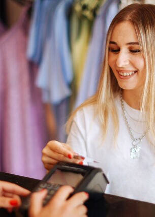Eine junge Frau bezahlt kontaktlos mit ihrer Kreditkarte an einem Kassentresen in einer Modeboutique