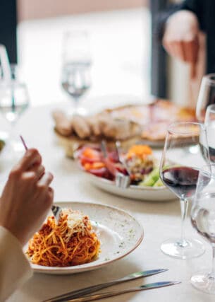 Eine Gruppe Personen an einem weiß eingedeckten Tisch in einem Restaurant mit verschiedenen Gerichten wie beispielsweise Pasta.