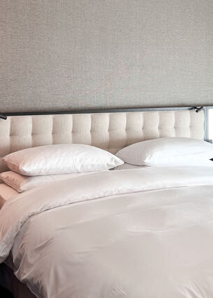 Doppelbett mit gepolstertem Kopfteil und Spiegeln sowie Nachttischen im modernen, minimalistischen Design vor einer grau tapezierten Wand.
