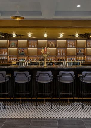Stilvolle Bar mit goldenem Dekor und gepolsterten Barhockern am Tresen.