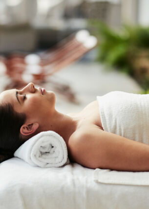 Eine Frau entspannt in einem weißen Handtuch auf einer Massageliege an einem Hotelpool.