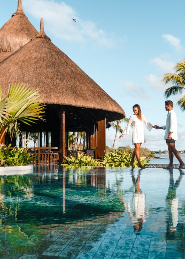 Ein Paar steht an einem luxuriösen Hotelpool am Meer in tropischer Umgebung.