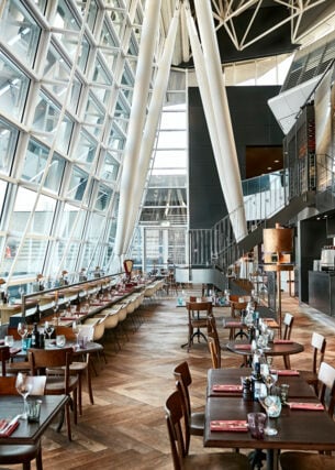 Eingedeckte Esstische eines stilvollen Restaurants mit Panoramafenstern in einem Flughafenterminal.