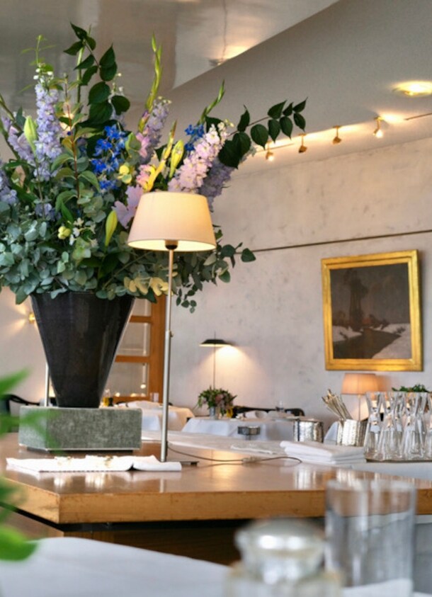 Innenraum des Restaurants Wielandshöhe mit einem Holztisch, weiß eingedeckten Tischen und Blumendeko.