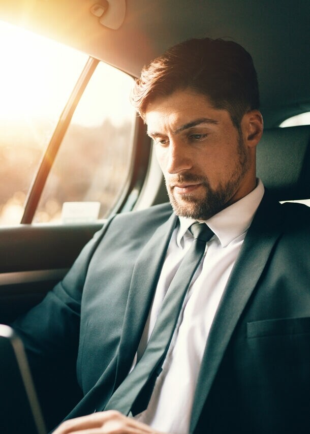 Ein Geschäftsmann sitzt mit Laptop auf dem Rücksitz eines Autos.