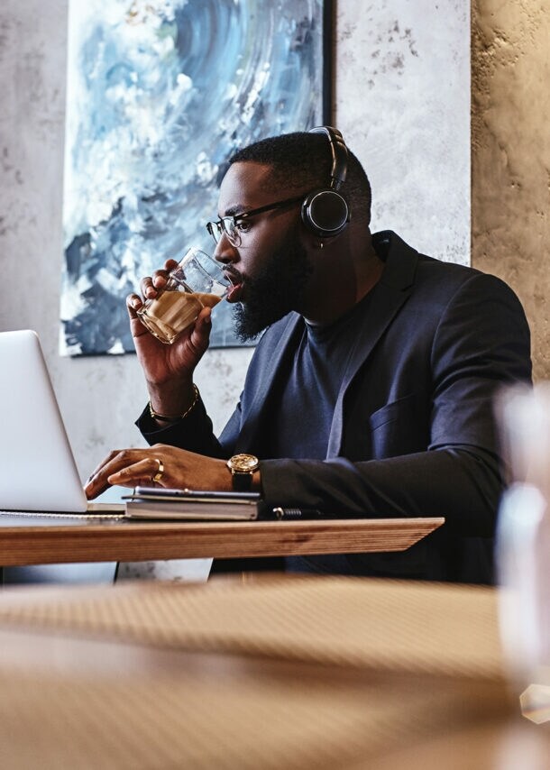 Ein Geschäftsmann mit Kopfhörer arbeitet in einer Hotellobby am Laptop.
