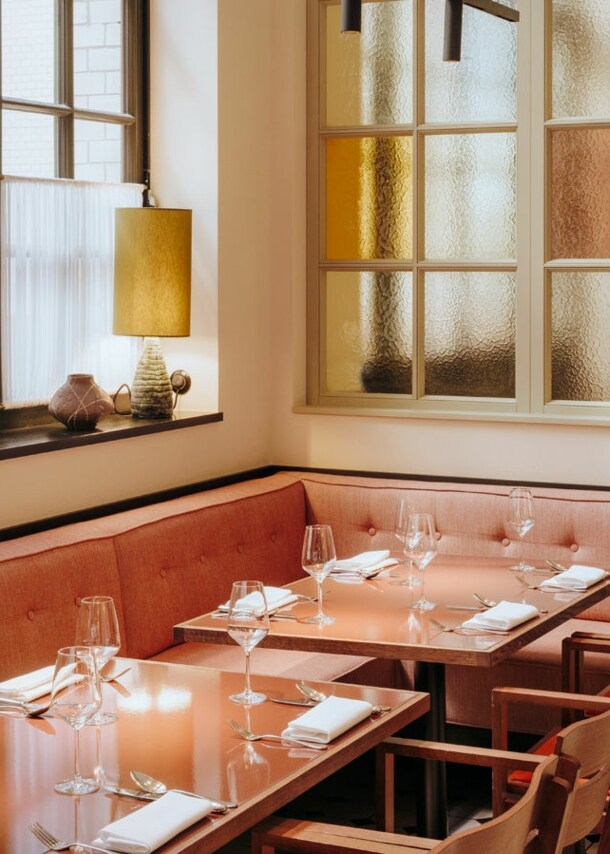 Interieur mit gedeckten Tischen und korallfarbenen Sitzmöbeln am Fenster.