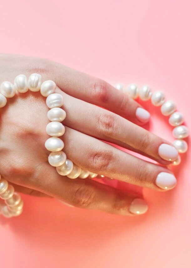 Eine Frauenhand mit Perlenkette umwickelt auf rosa Untergrund