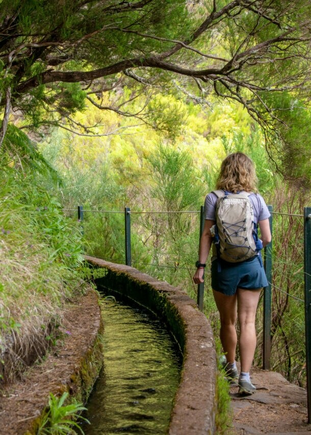 Rückansicht einer Frau auf einem Wanderweg auf Madeira, der entlang eines Bewässerungskanals verläuft.