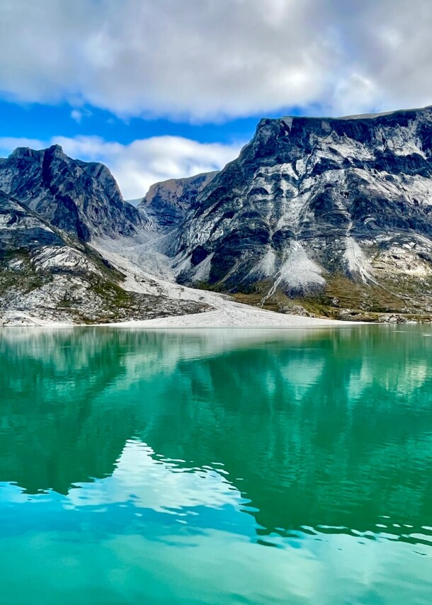 Das Bild zeigt dunkle Berge, die aus dem grün schimmernden Wasser des Prins Christian Sunds ragen. 