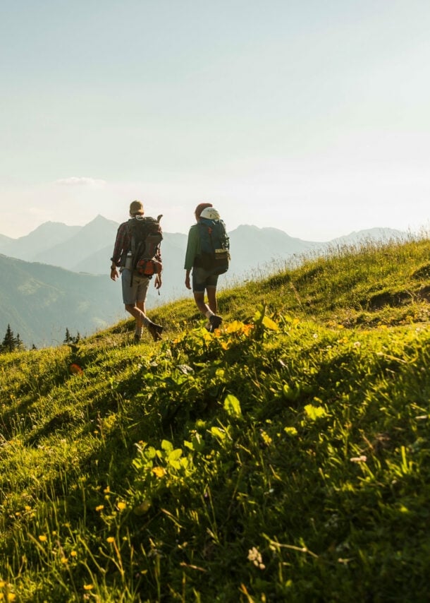 Rückenansicht von zwei Personen, die über eine Bergwiese in Österreich wandern.