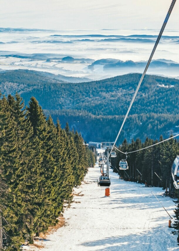 Skilift, der im Riesengebirge über eine Skipiste und Wald verläuft, im Hintergrund Berge.