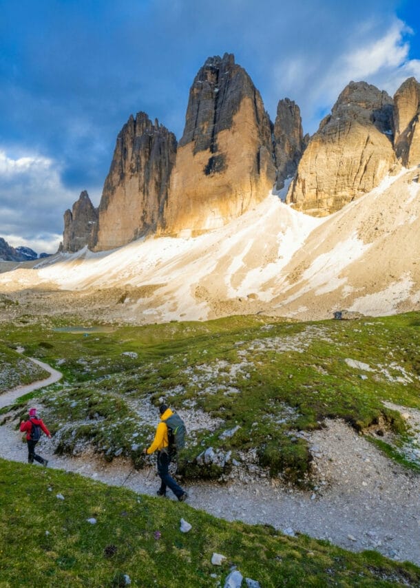 Zwei Personen beim Wandern, im Hintergrund Berge, blauer Himmel und Wolken.