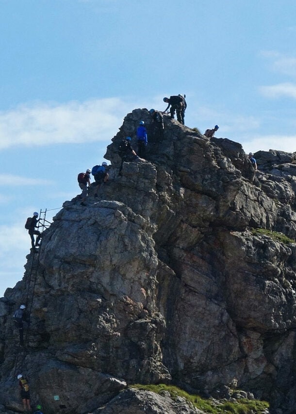 Mehrere Personen, die einen Felsen am Hindelanger Klettersteig erklimmen.