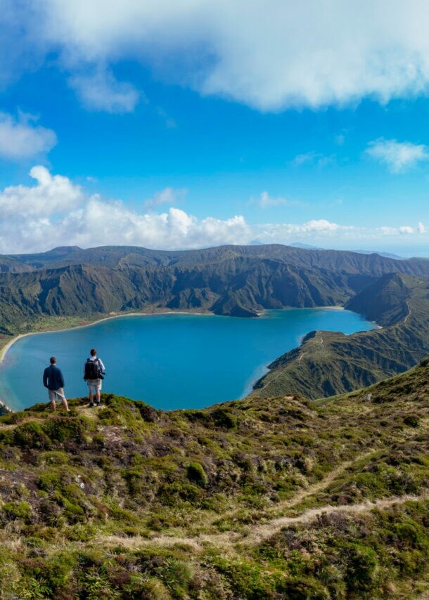 Rückansicht von zwei Personen, die auf einem Hügel stehen mit Blick auf einen See.