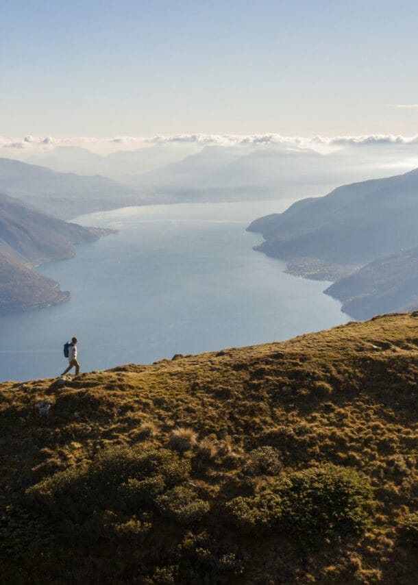 Panoramaaufnahme von einem Mann mit Rucksack auf einem Berg und dem Lago Maggiore im Hintergrund.