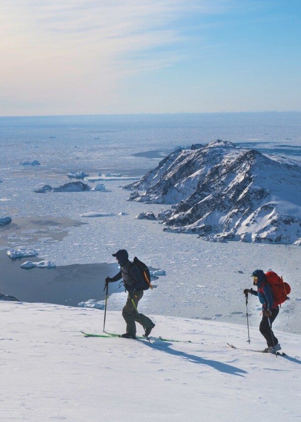 Drei Personen auf Skiern laufen einen schneebedeckten Bergkamm vor einer Gletscherlandschaft entlang.