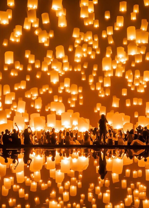 Unkenntliche Personen, die gleichzeitig im Dunkeln unzählige leuchtende Laternen in den Himmel schweben lassen.