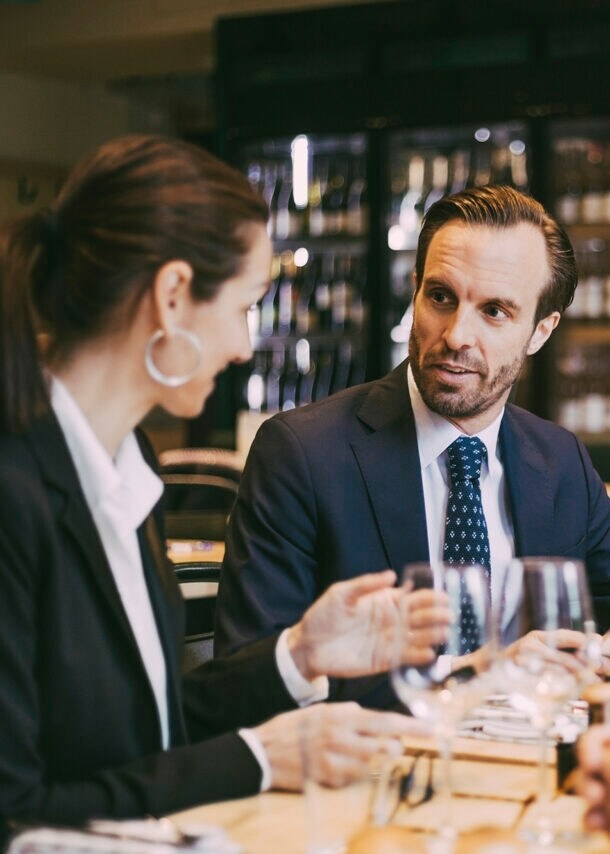 Mehrere Personen sitzen beim Business Lunch im gemütlichen italienischen Restaurant: Sie speisen und sind mitten im Small Talk.