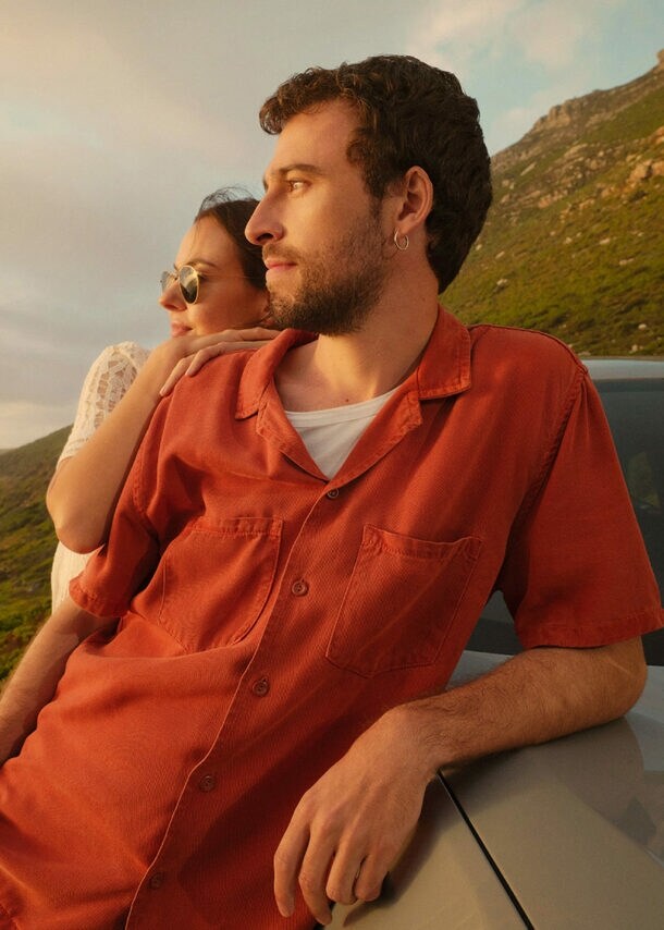 Ein Paar lehnt seitlich an einem Auto an einer Küste und blickt aufs Meer.