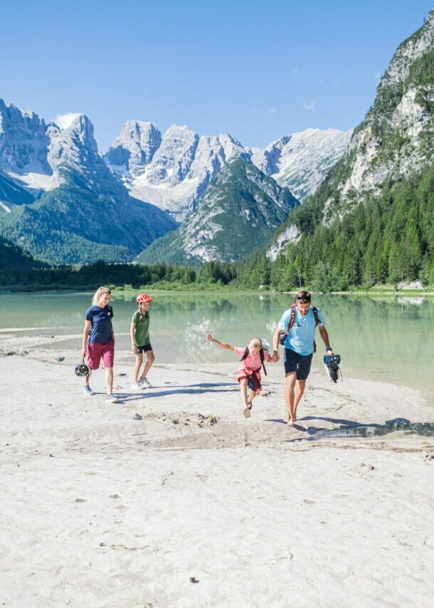Eine Familie mit zwei Kindern in sommerlicher Sportkleidung läuft an einem See in den Bergen entlang.
