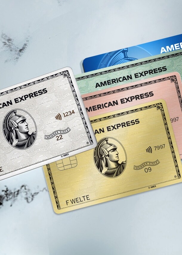 Eine Hand hält eine American Express Platinum Kreditkarte über drei weitere Kreditkarten in unterschiedlichen Farben auf einem Marmortisch.