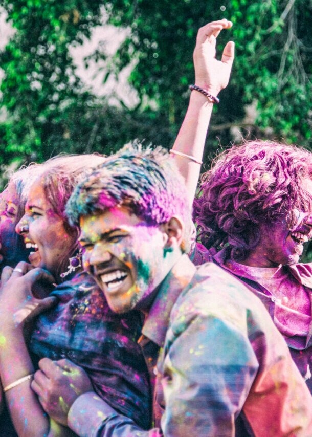 Lachende Personen indischer Abstammung voll mit bunter Farbe auf einem Holi Festival.