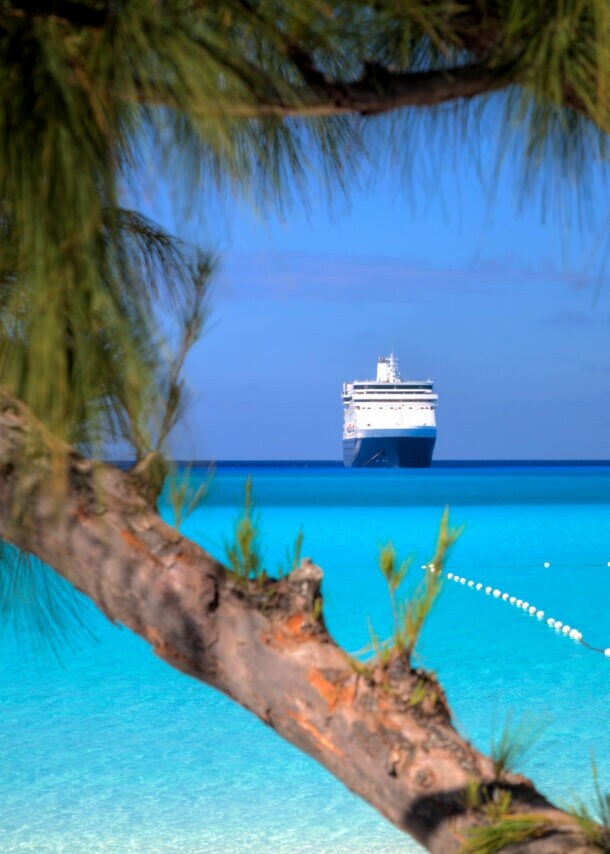 Kreuzfahrtschiff am Horizont eines Karibikstrands mit klarem türkisfarbenem Wasser.