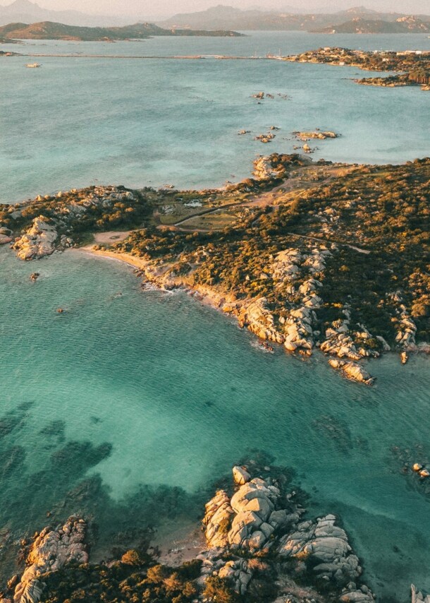 Luftaufnahme einer felsigen Küstenlinie mit klarem, türkisfarbenem Wasser und kleinen Buchten bei Sonnenuntergang.