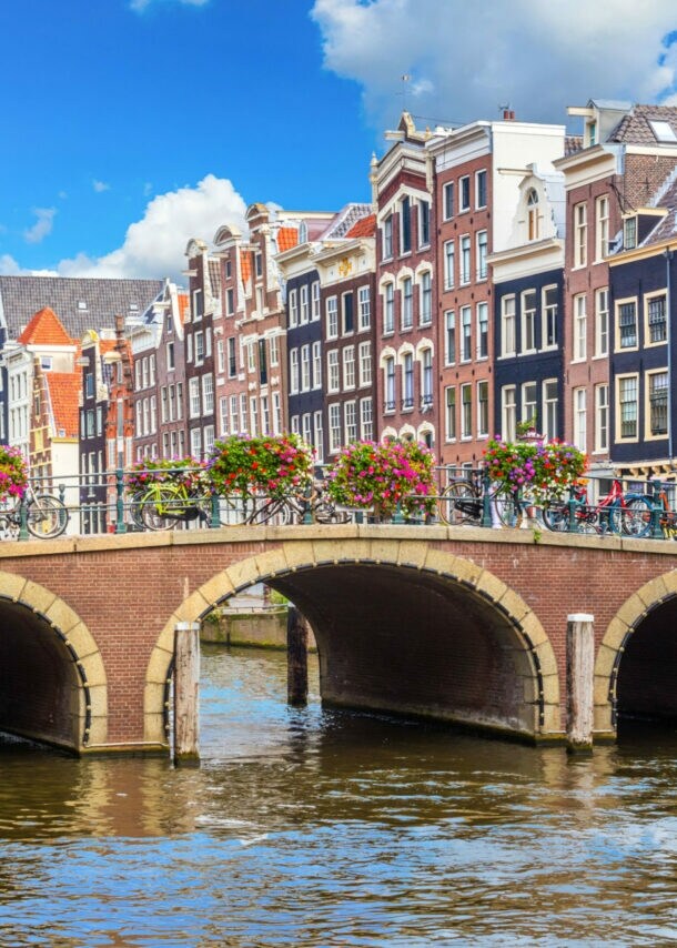 Eine mit Blumen geschmückte Steinbrücke über einem Kanal vor einer Reihe Grachtenhäuser im Stadtzentrum von Amsterdam.