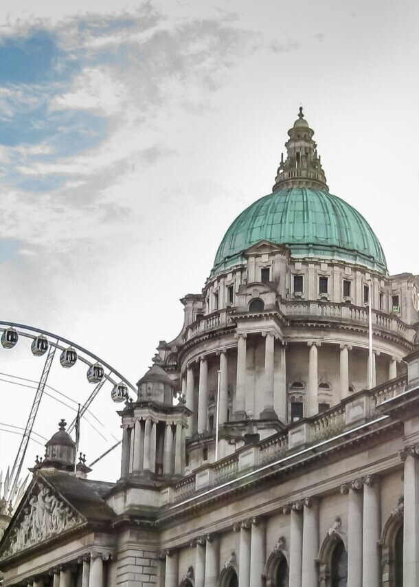 Historisches Gebäude mit grüner Kuppel und Riesenrad im Hintergrund bei Sonnenlicht