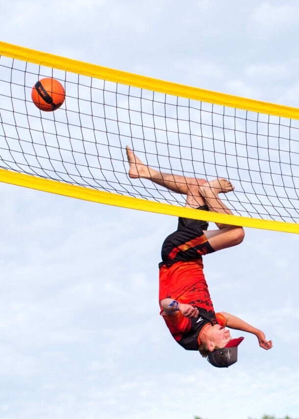 Ein Sportler kopfüber bei einem Sprung an einem Volleyballnetz, daneben ein fliegender Ball.