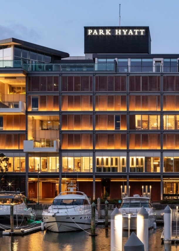 Das warme Licht des Park Hyatt Hotels spiegelt sich im Hafenbecken von Auckland, während die weißen Yachten direkt davor vor Anker liegen.