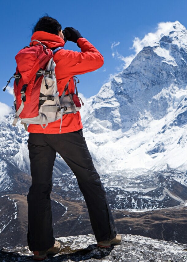 Ein Wanderer in roter Jacke blickt auf einen schneebedeckten Berggipfel im Himalaja