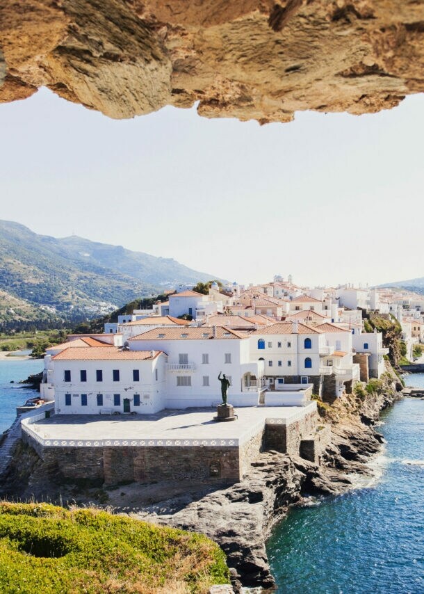 Blick auf weiße Häuser eines Ortes auf einer felsigen Landzunge im Meer durch ein Loch in einer Felsenmauer.
