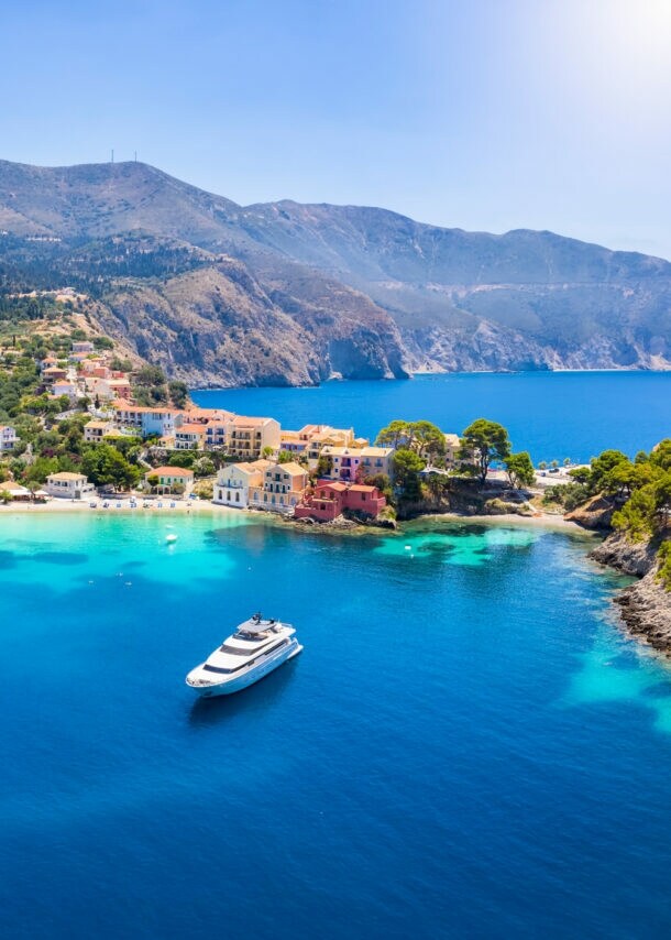 Kleiner Küstenort mit weißen Häusern, umgeben von grünen Hügeln und Bergen, mit klarem blauem Meer und einem Boot im Hafen