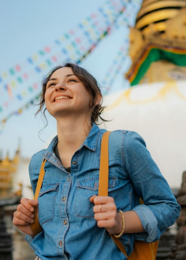 Eine junge, lächelnde Frau mit Rucksack vor einem nepalesischen Tempel.