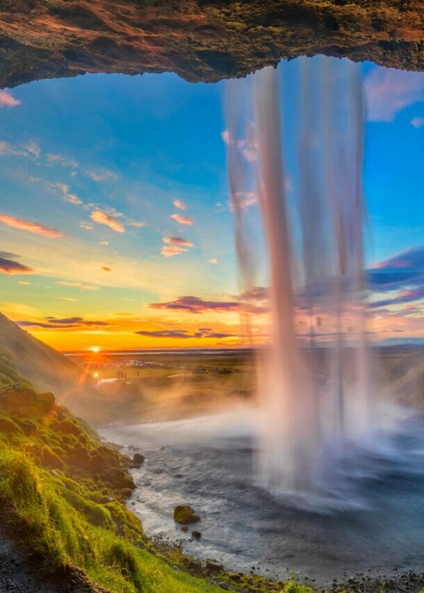 Wasserfall, der von einer Höhle aus bei Sonnenuntergang in eine grüne Landschaft fällt
