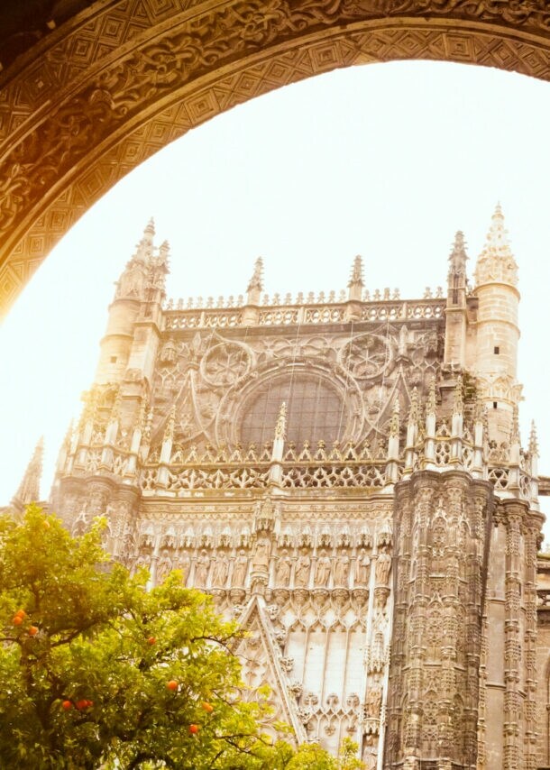 Gotische Kathedrale mit detaillierten Steinmetzarbeiten, gesehen durch einen verzierten Bogenrahmen bei Sonnenlicht