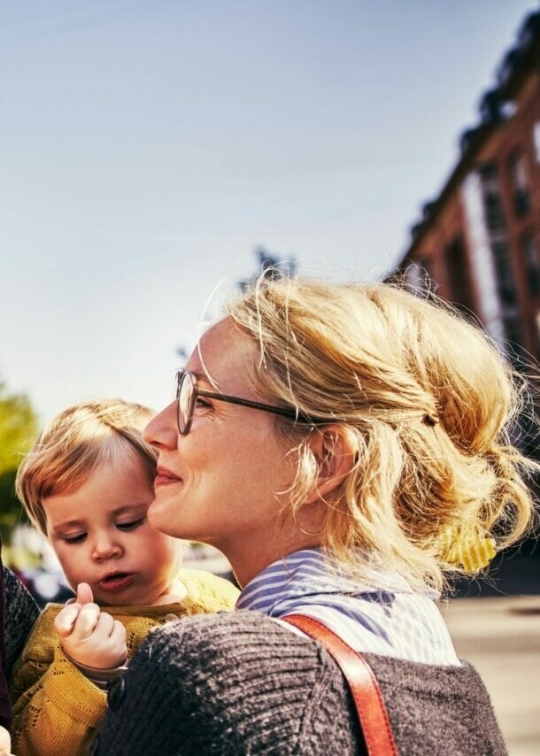 Vater trägt lachendes Kleinkind auf Schultern, Mutter mit Brille schaut liebevoll, während sie ein weiteres Kleinkind im Arm hat.