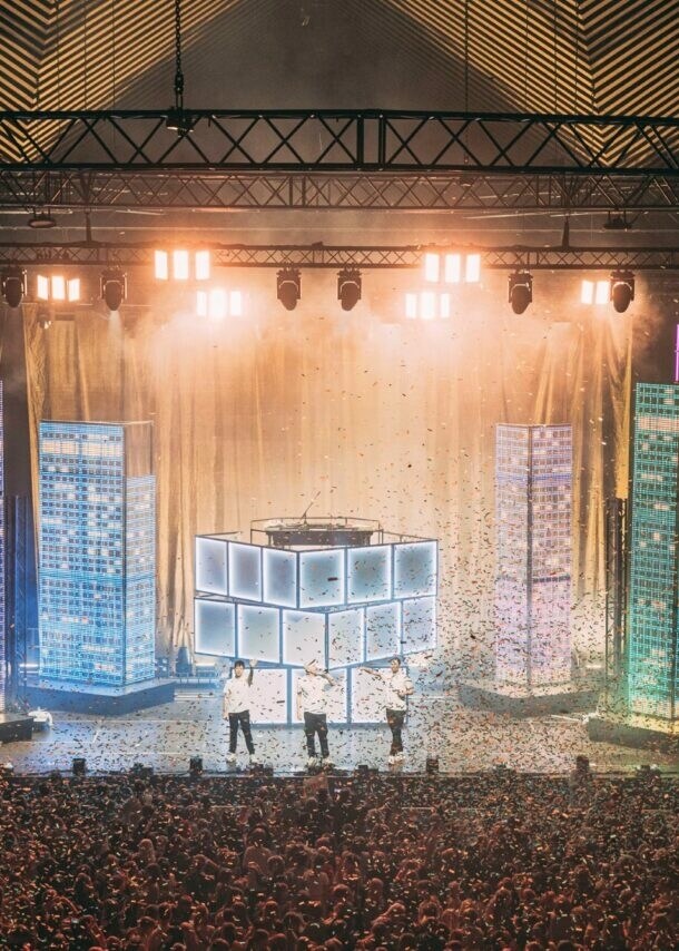 Große Menschenmenge bei einem Konzert oder Event in einer Halle mit beleuchtetem Bühnenbereich und Nebeleffekten.