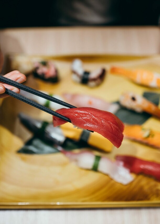 Eine Hand mit Stäbchen über einem Teller mit verschiedenen Sushi-Sorten.