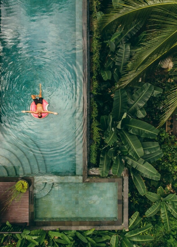 Junger Mann auf einer Luftmatratze in einem Infinity-Pool mit tropischer Umgebung.