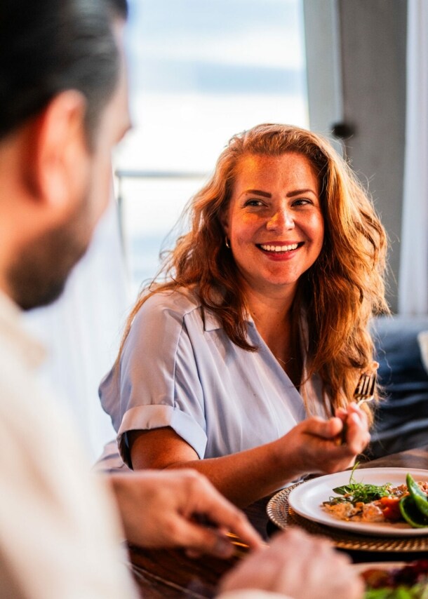 Eine lächelnde Frau im Restaurant sitzt einem Mann gegenüber, zwischen ihnen steht ein hübsch angerichteter Teller.