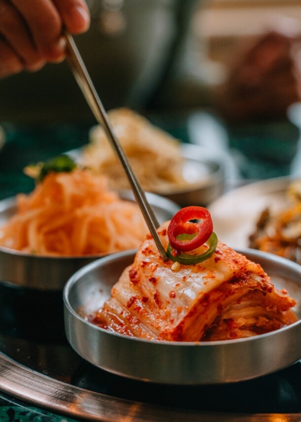 Eine Hand stippt Essstäbchen in eine Schale mit fermentiertem Kohl auf einem Tisch in einem Restaurant.