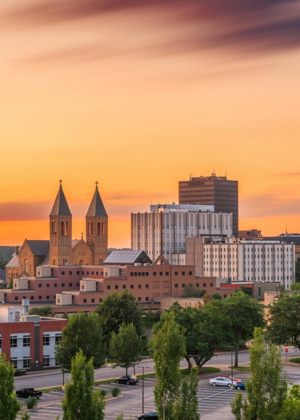 Stadtansicht von Akron bei Sonnenuntergang mit Gebäuden, zwei Kirchtürmen und Bäumen im Vordergrund