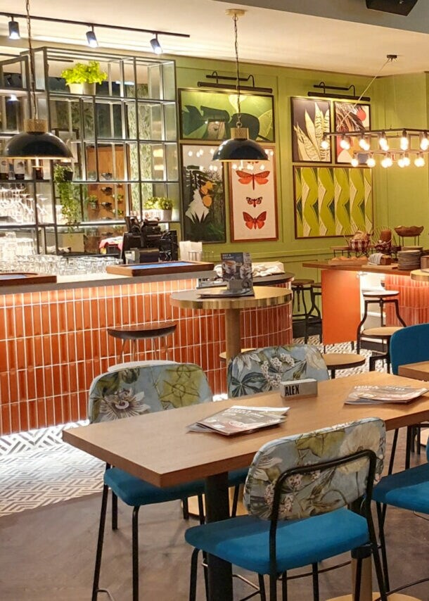 Innenansicht des ALEX in Ludwigshafen, mit Holztischen, bunten Stühlen und dekorativen Bildern an der Wand.