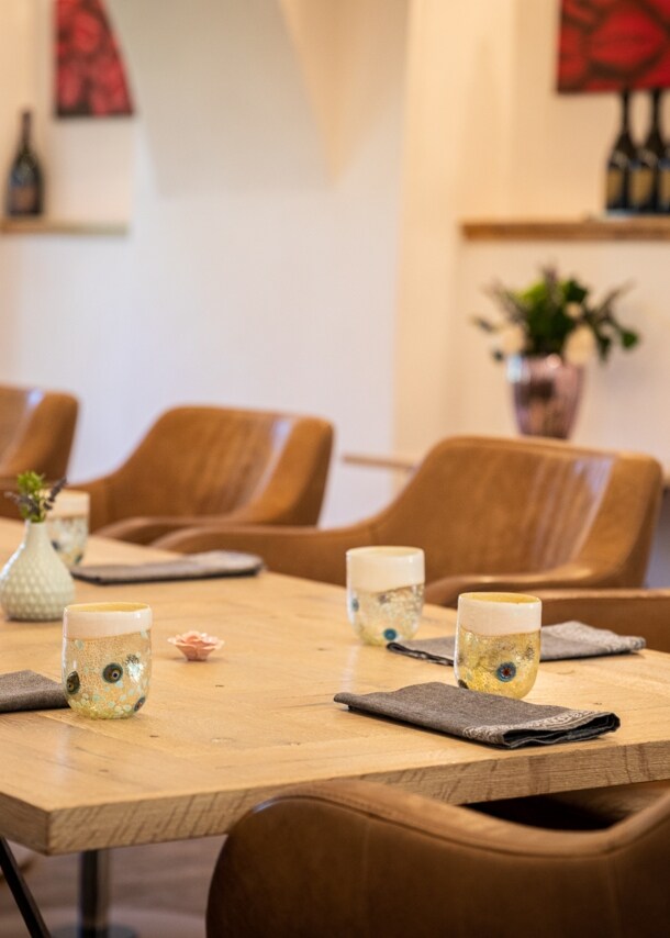 Gedeckte Holztische an denen cognacfarbenen Ledersessel stehen eines Sternerestaurants, im Hintergrund stehen Champagnerflaschen auf Regalen.